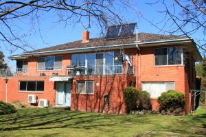 A sun lit two story brick home stands against a brilliant blue sky