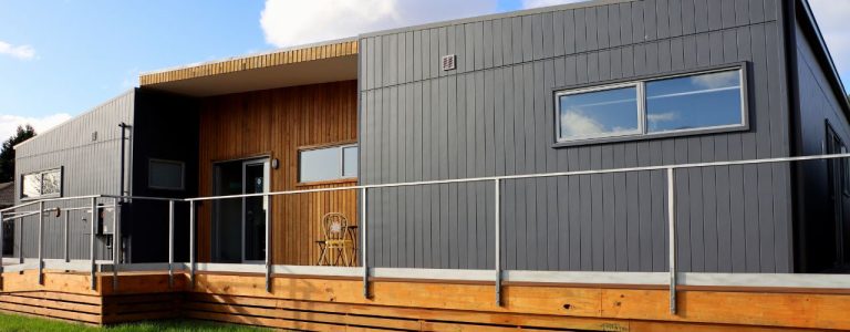 Modern wheelchair accessible home with a stylish exterior, featuring a wooden deck, large windows, and a welcoming entrance, set in a tranquil environment near Berriedale, Tasmania.